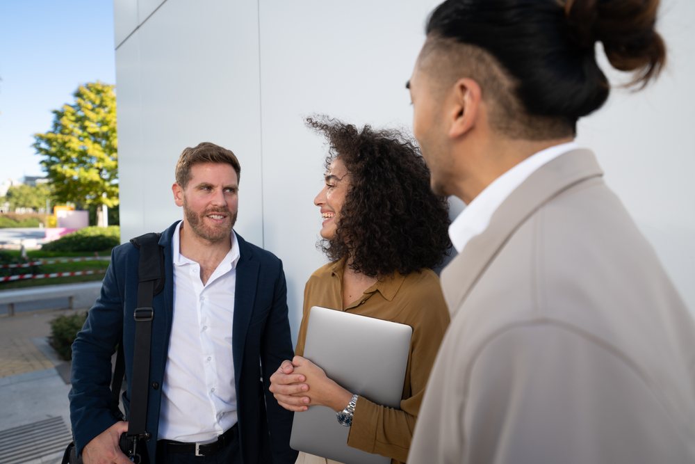Three colleagues in business casual attire engage in an outdoor conversation near a modern building during daylight, Madrid, Spain.