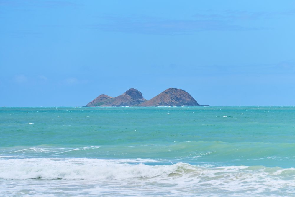 Island in the distance across ocean water with visible waves under a clear blue sky, Hawaii, USA.