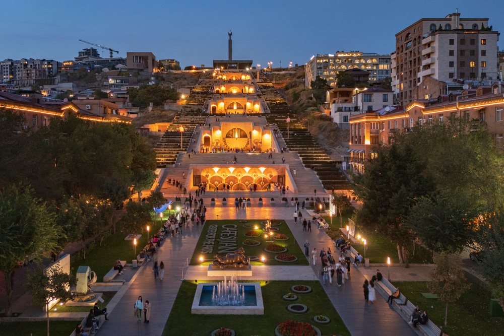 The Cascade stairway landmark illuminated at dusk with people walking and gathering around fountains and gardens, Yerevan, Armenia.