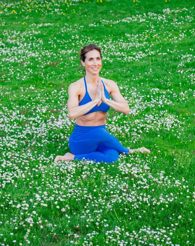 Woman practices yoga meditation outdoors while sitting cross-legged in a wildflower field, USA.