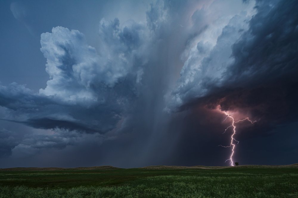 Lightning strikes illuminate storm clouds over grassland in the Nebraska Sandhills near Dunning during Blue Hour, Storm Chasing, Weather, Environmental Issues, USA.