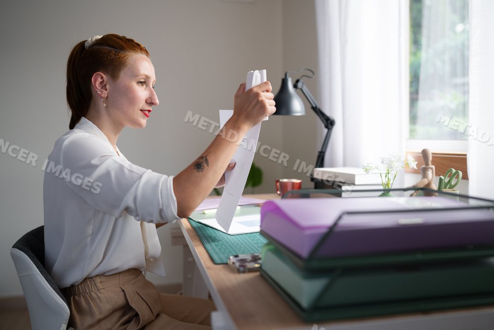 A white woman staples papers while working from home in Galicia, spain