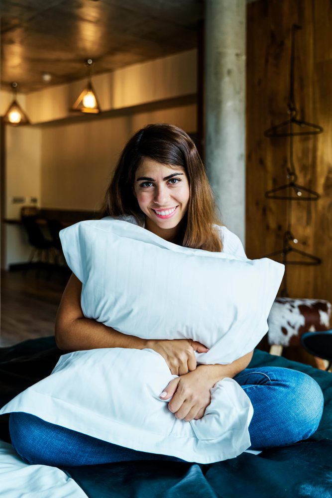 A young woman sitting cross-legged and hugging a pillow