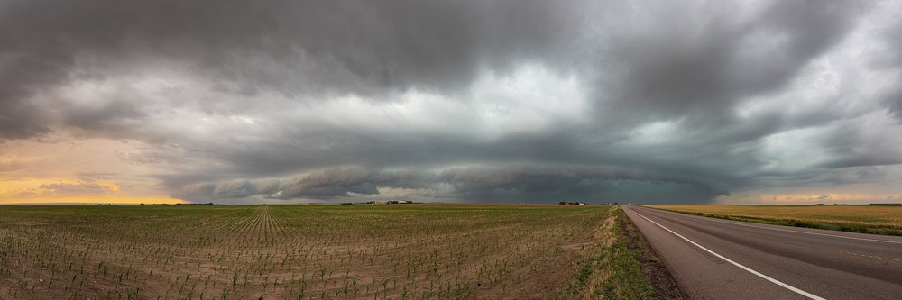 Storm with a visible mesocyclone moves over open farmland along Colorado Highway 14 in the Great Plains of the USA at sunset, Tornado Alley.