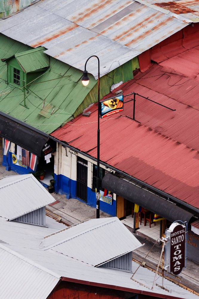 Rooftops with corrugated metal roofs, a street lamp, and illuminated Hotel Santo Tomas sign above a restaurant entrance, San Jose, Costa Rica.