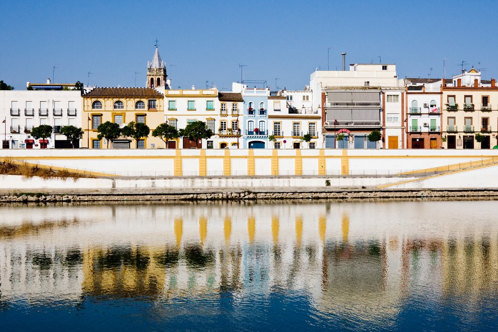 Buildings along the Guadalquivir River, Spain reflect in the water under a clear blue sky, Andalusia.