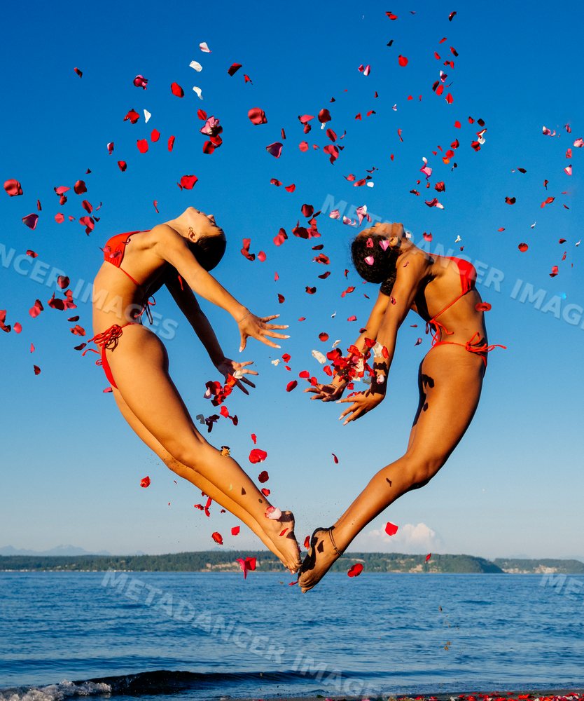Two women jump gracefully with flower petals on a beach in WA, USA