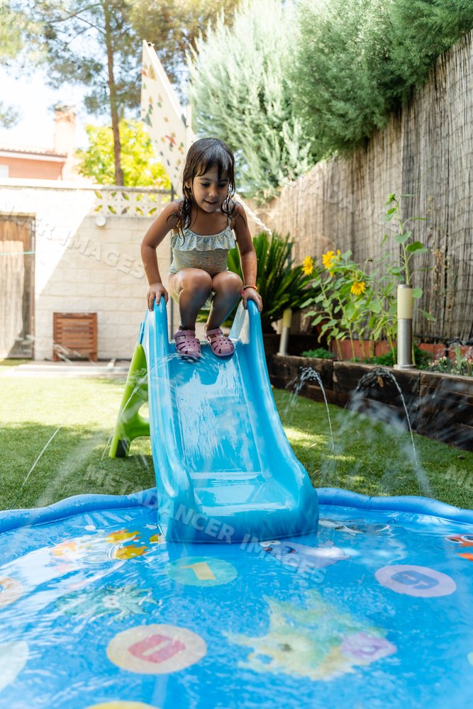 Young white girl having fun on a blue water slide in a sunny backyard