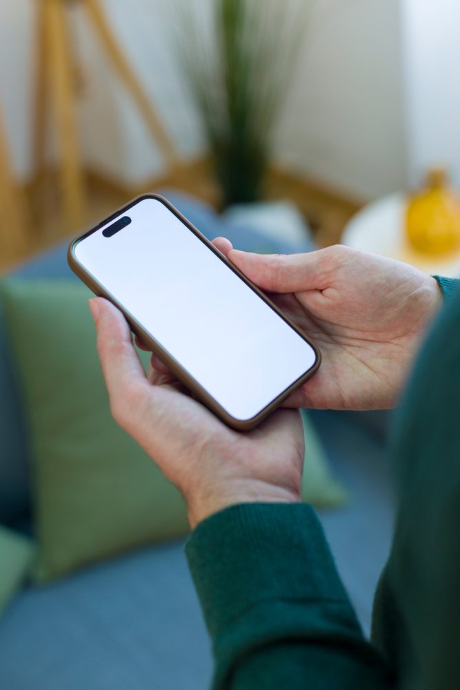 Person holding a smartphone with a blank screen indoors, Technology, young adult, home.