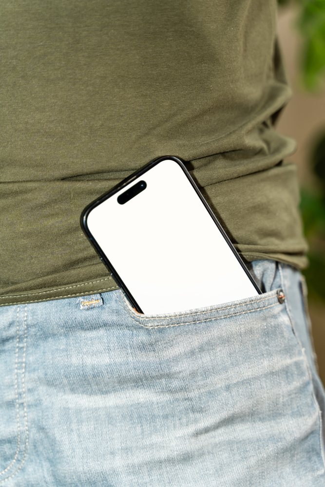 Close-up of a smartphone inserted in a jeans pocket worn by a person in a green shirt and blue jeans, mock up, white screen, Spain.