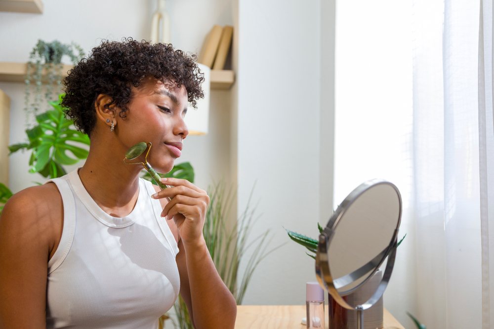 Woman using a jade roller on her face at a vanity table, Young woman, home.