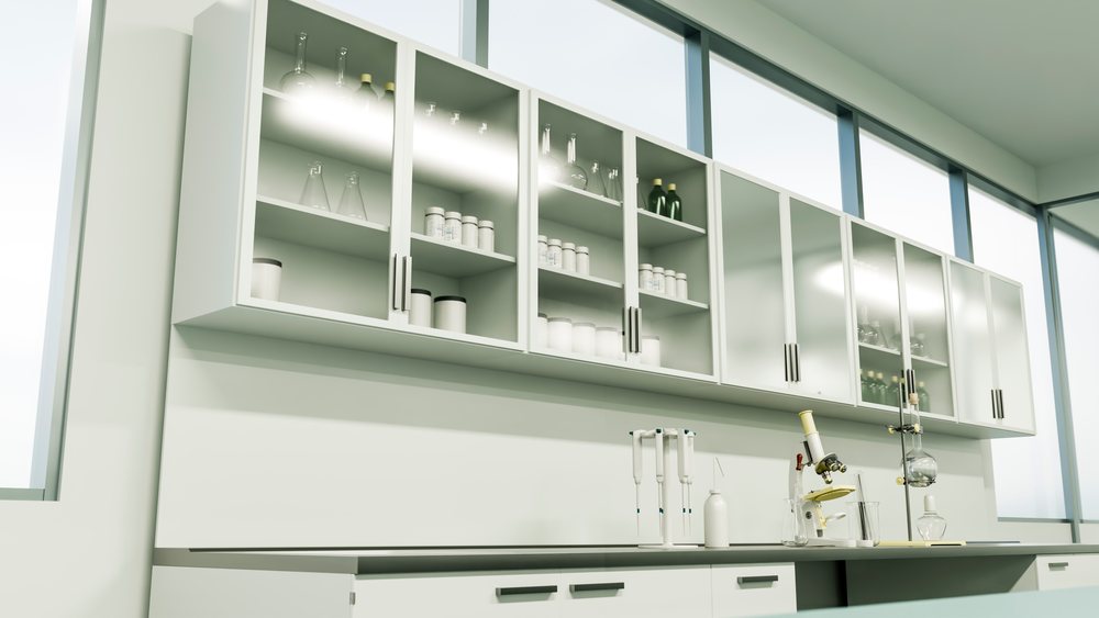 Laboratory workspace with microscope, pipettes, and glassware on a countertop beneath white cabinets filled with test bottles and glass containers.