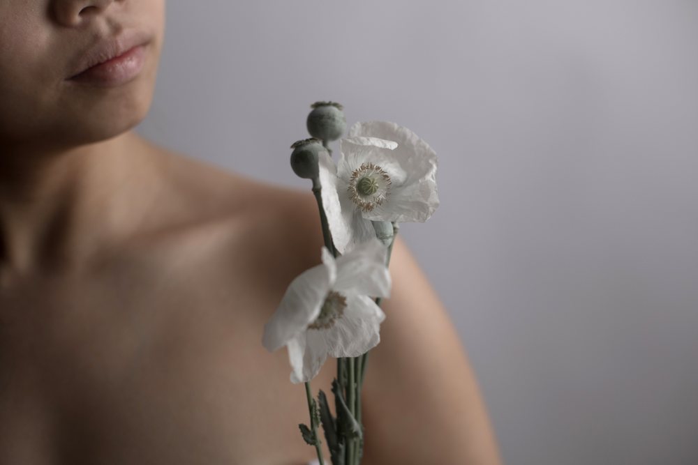Woman holding white poppy flowers with buds against a gray background in a serene portrait, Art, emotional.