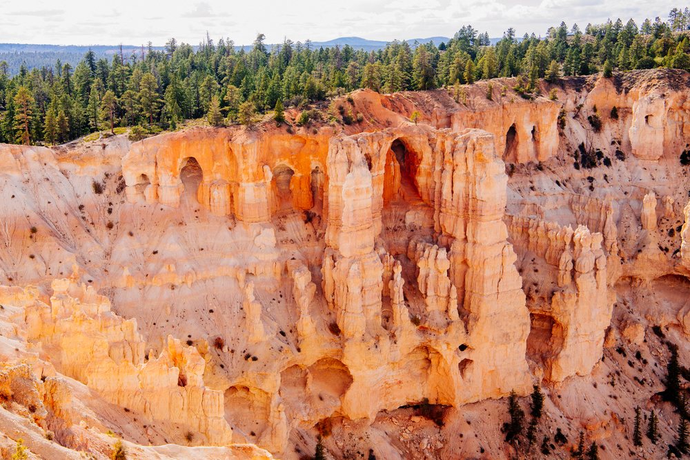 Rock formations and orange sandstone cliffs rise amid forest and distant hills in Bryce Canyon National Park, Utah, USA.