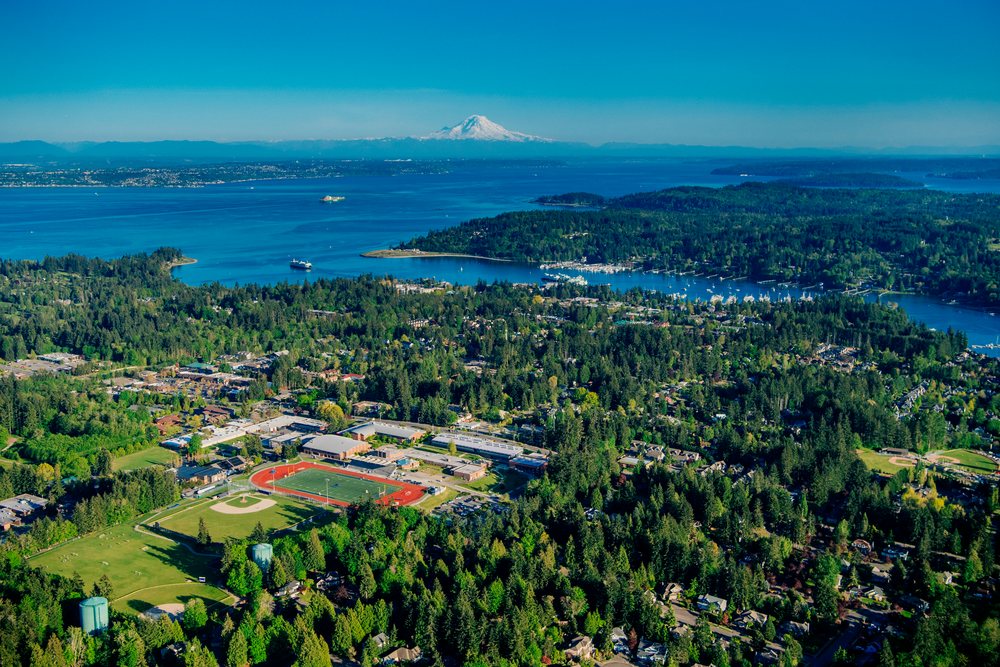 Aerial view of Eagle Harbor and Bainbridge Island with snow-capped mountain over Puget Sound under a clear blue sky, Salish Sea, USA.