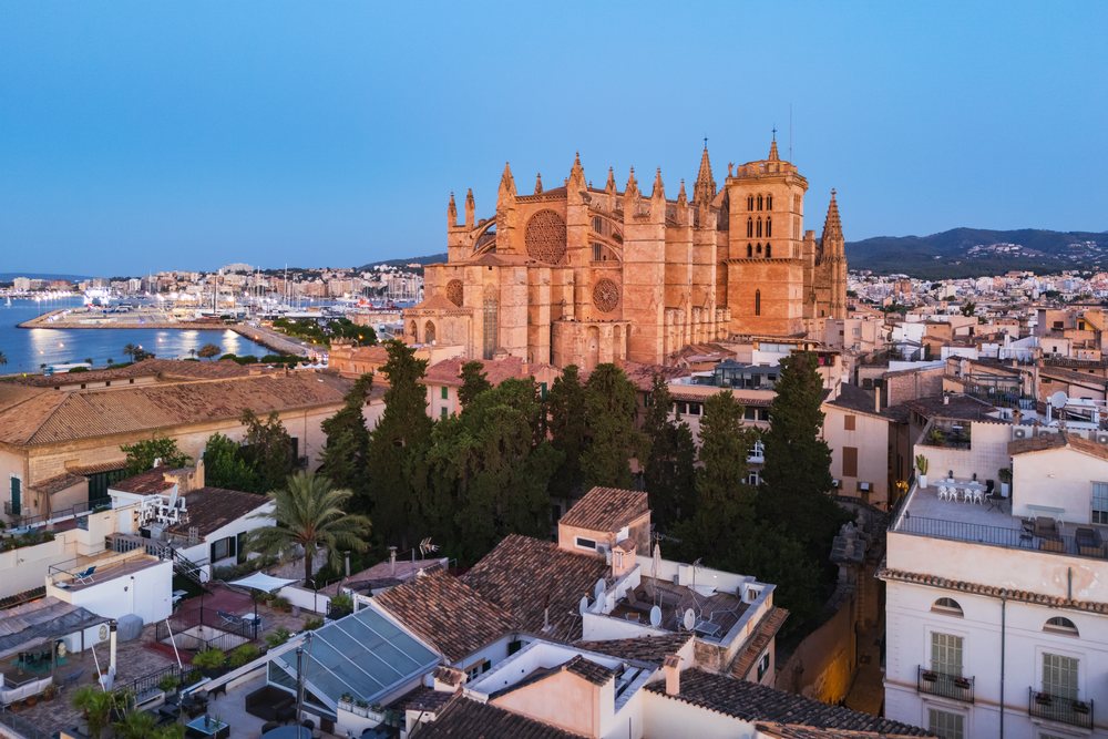 Cathedral in Palma de Mallorca illuminated at dusk overlooking harbor boats and city rooftops, Landscape, Lifestyle, Balearic Islands, Spain.