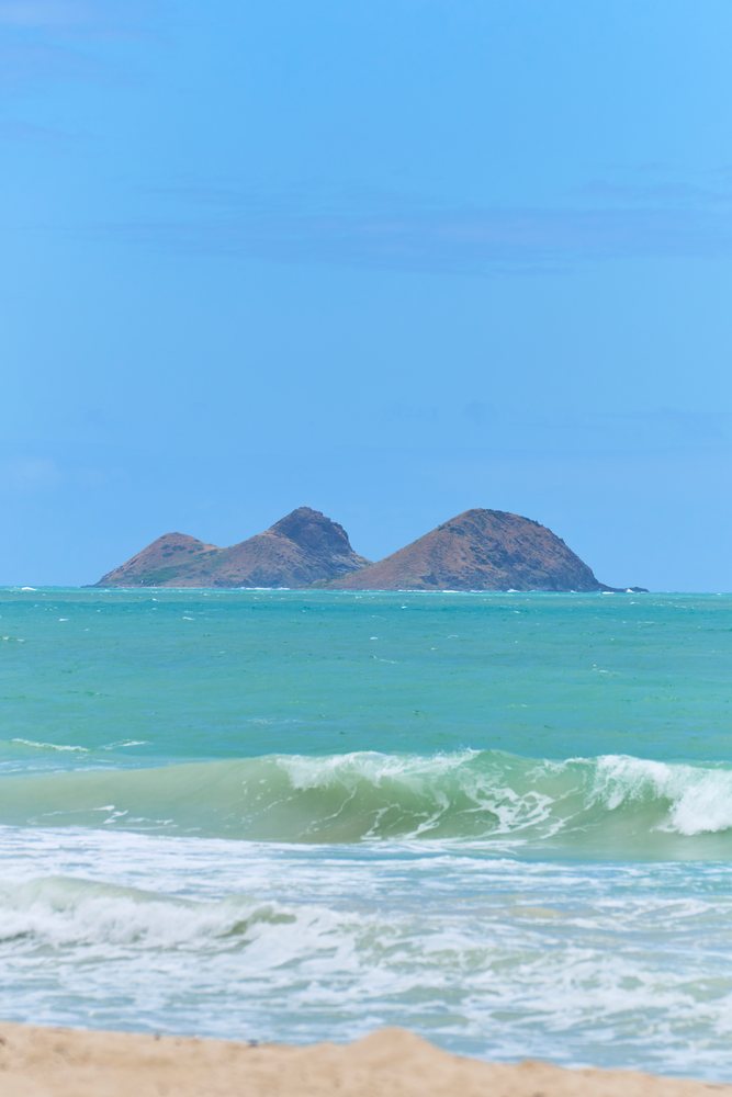Ocean waves break near a sandy beach with distant islands under a clear blue sky, Hawaii, USA.