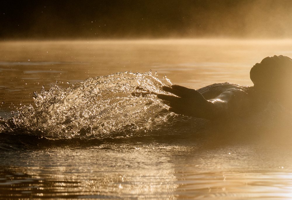Person floating in calm water creating a splash under golden light at sunset, USA.