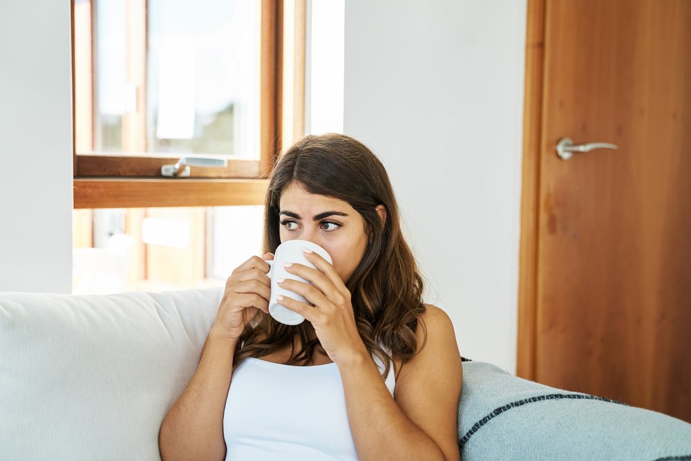 A young white woman drinks coffee on a couch inside a home in Iceland