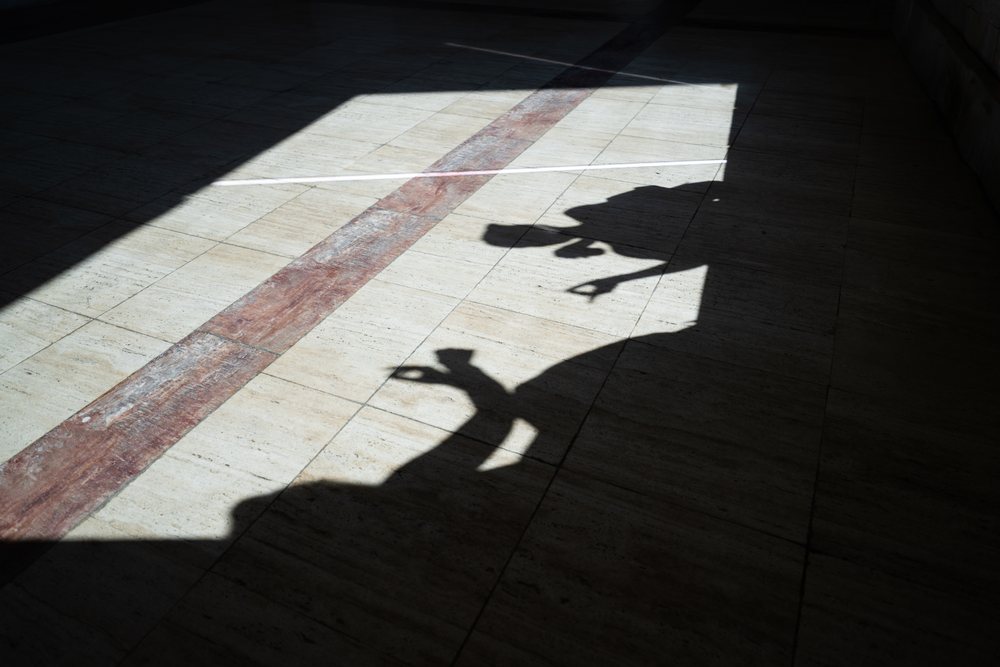 Shadows of two people displaying hand gestures on a brown and beige tiled indoor floor with contrasting sunlight and shadow, businesswomen, Spain.