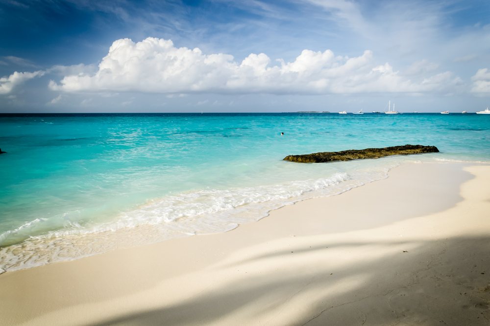 Beach shore with clear turquoise ocean waves, sand, and a rock under partly cloudy sky in Maldives landscape, summer, Holliday, travel, landscape.