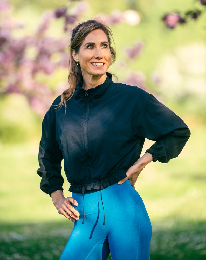 Woman in sportswear performs calisthenics outdoors on green grass with trees and sunlight, USA.