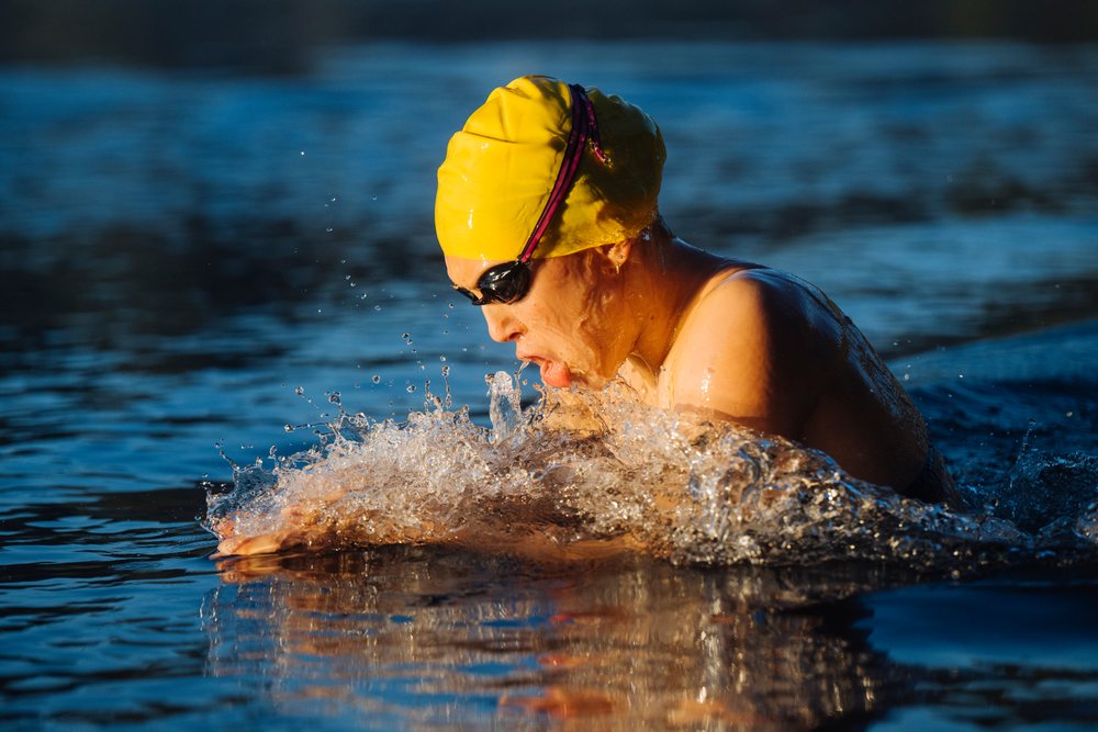 Swimmer performing breaststroke in open water wearing a yellow cap and goggles, USA.