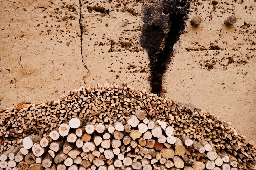 Stack of cut firewood arranged against a cracked beige wall, Shaanxi Province, China.