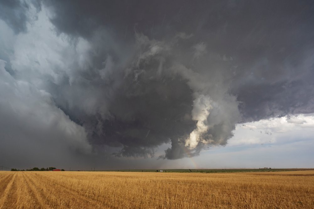 Supercell storm with dark clouds, rain, and rainbow over a dry harvested field, Levelland, Texas, USA.
