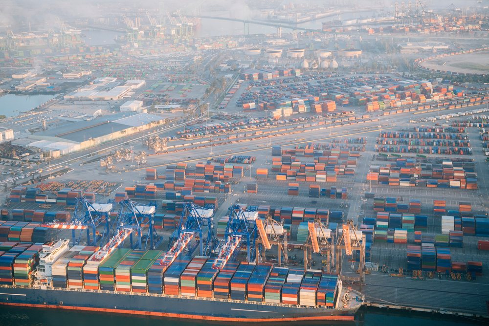 Container ship loaded with colorful shipping containers at the Port of Long Beach during cargo handling with cranes and stacked containers in the industrial port area, CA, USA.