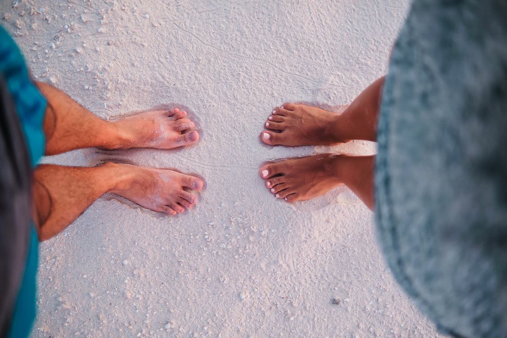 Bare feet of a couple standing on white sand at a beach in the, Maldives.
