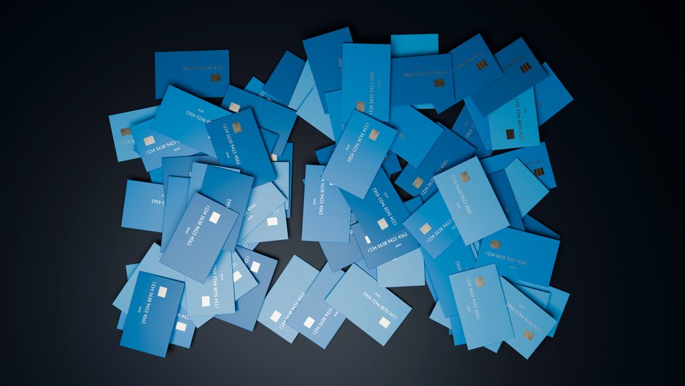 Pile of overlapping blue credit cards with visible chips and numbers on a dark background.