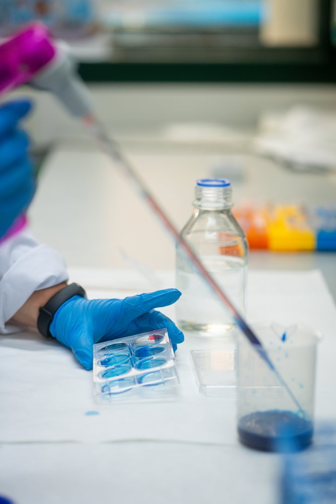 Scientist in Seville laboratory transferring blue liquid with pipette into test tray for research purposes, Andalucía.