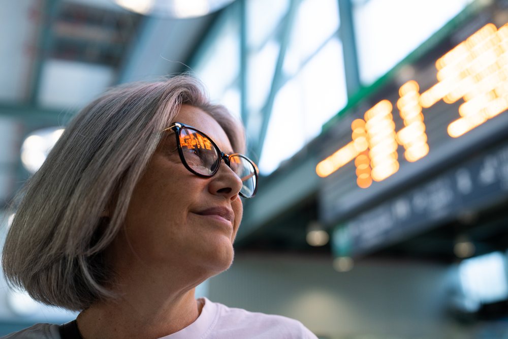 Woman with grey hair and glasses looking sideways inside a modern building with reflected lights on her lenses, Spain.