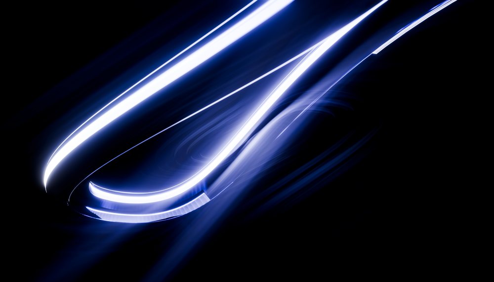 Close-up of vehicle headlights illuminating with bright blue LED light against a dark background.