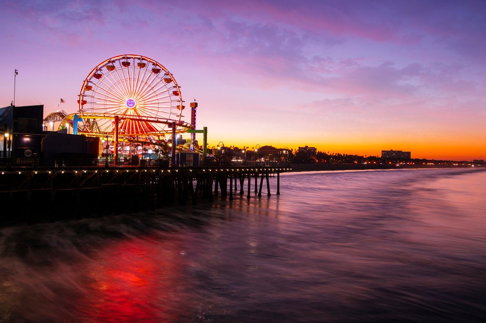 Sunset with illuminated Ferris wheel reflecting on the Pacific Ocean at Santa Monica Pier, lifornia, CA, USA.