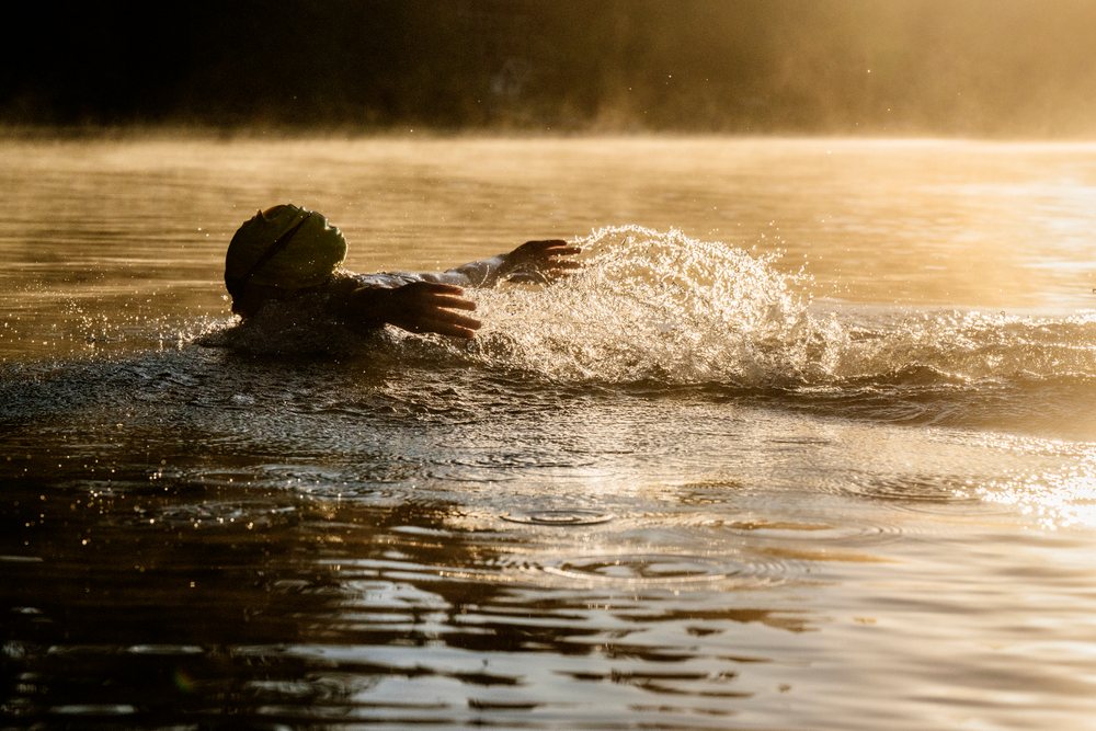 Swimmer performing backstroke in open water during early morning light, USA.