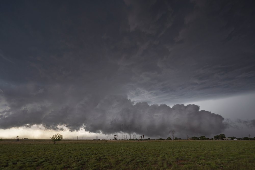 Large dark storm cloud moves over a grassy open field with oil pump jacks and power lines in Tornado Alley, Levelland, Texas, USA.
