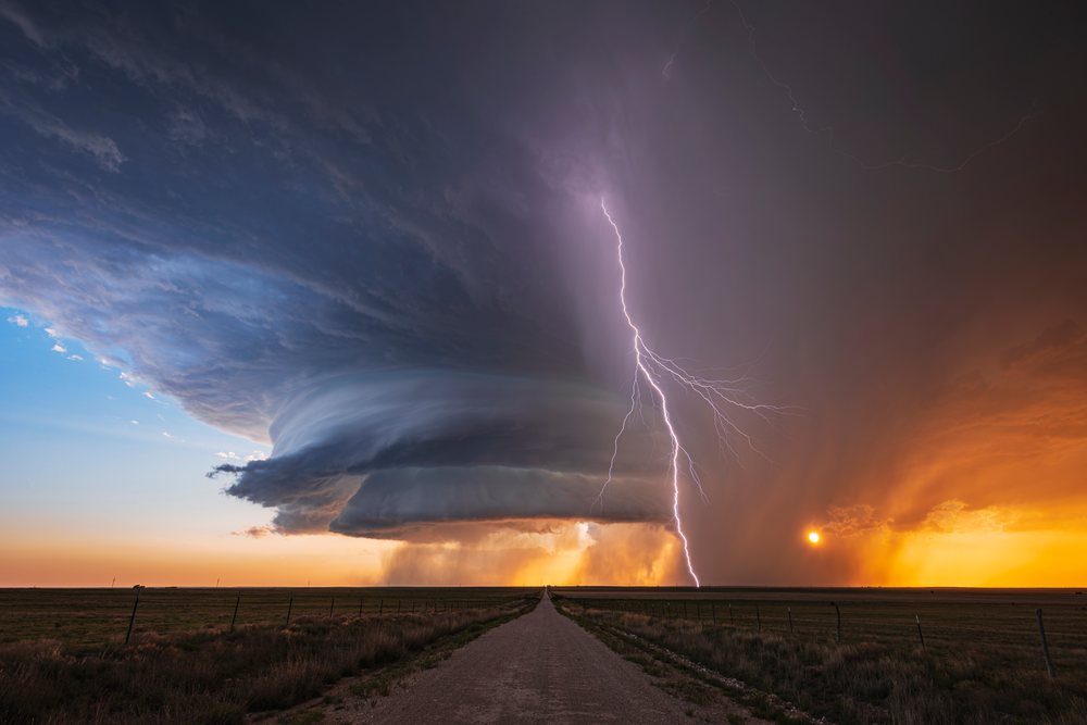 Supercell storm with Lightning strikes over an open dirt road at sunset in grassland of New Mexico, in Tornado Alley of the Great Plains, Amistad, USA.