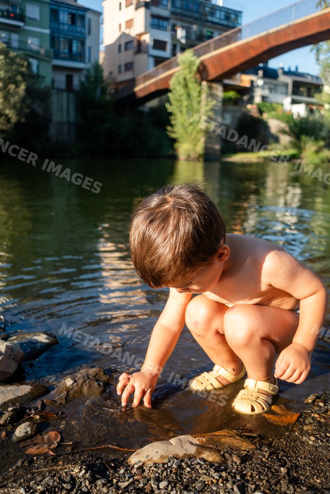 A young white boy playing with water and rocks at a riverbank in Spain