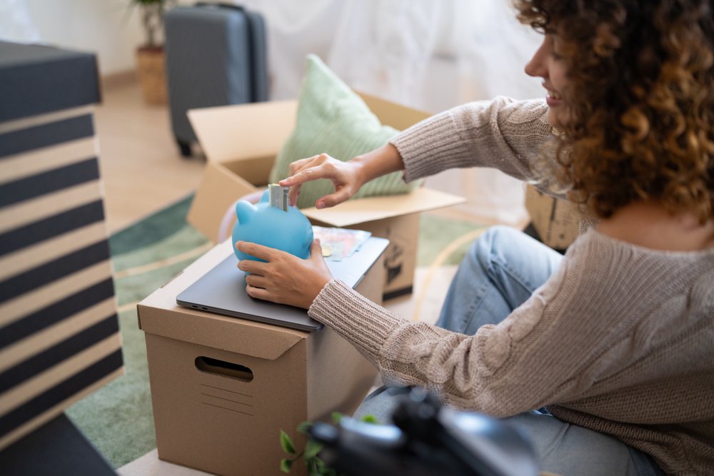 Woman inserts card into blue piggy bank while sitting on floor, moving, Spain.