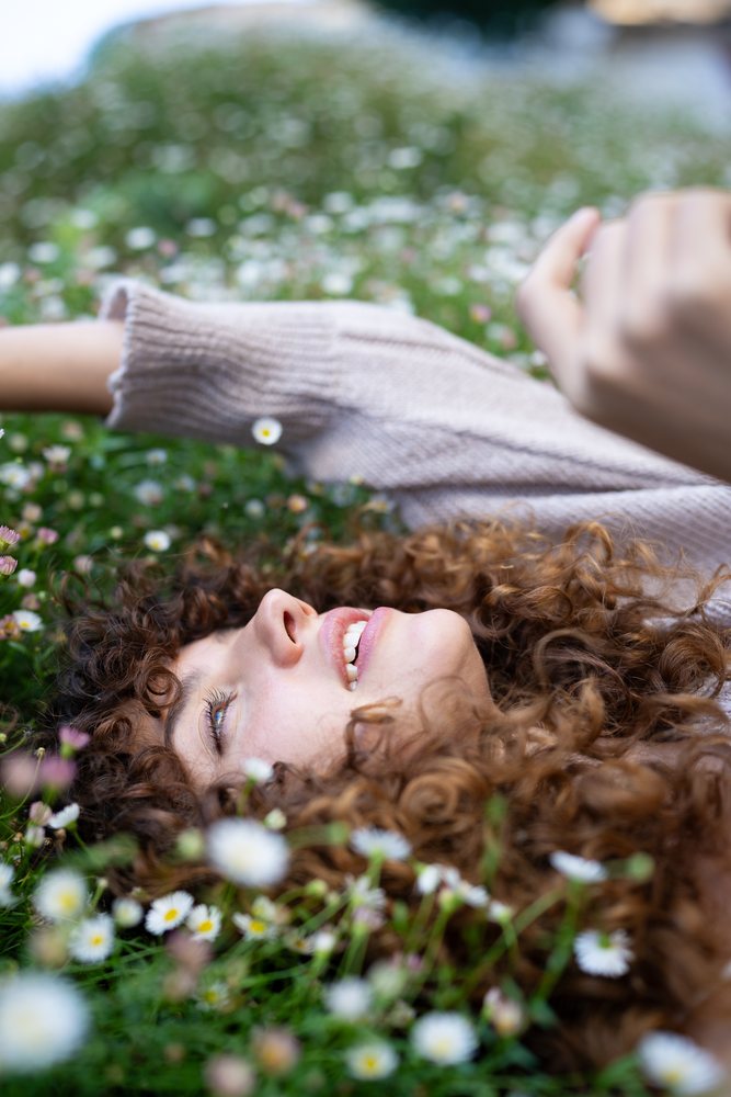 Woman with curly hair lies in a blooming daisy field outdoors, enjoying a serene spring day, home story, influencer, Spain.