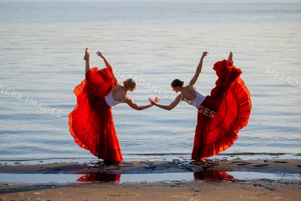 Two white women practicing partner acrobatics yoga on a beach