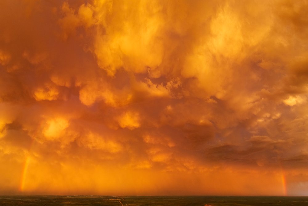 Rainbow appears beneath dramatic dark orange storm clouds at Sunset over the flat landscape of Uvalde in the Great Plains, Storm Chasing, Weather, Environment, Texas, USA.
