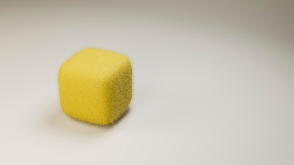 Yellow furry cube with rounded edges rendered in 3D on a minimalist studio background with soft shadow.
