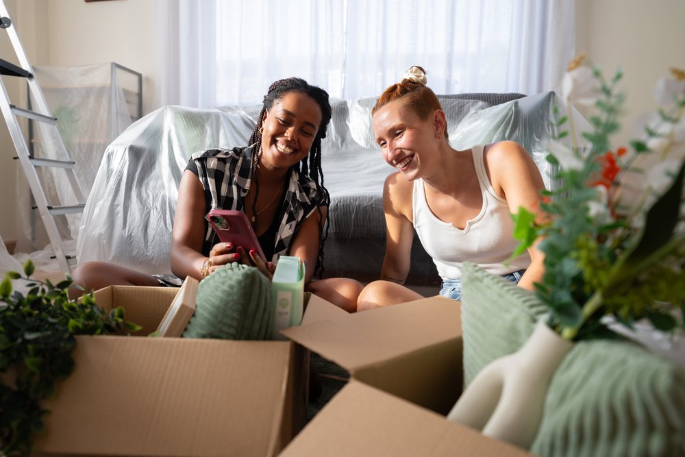Two women unpack boxes and smile together in a living room during a move, moving, Spain.