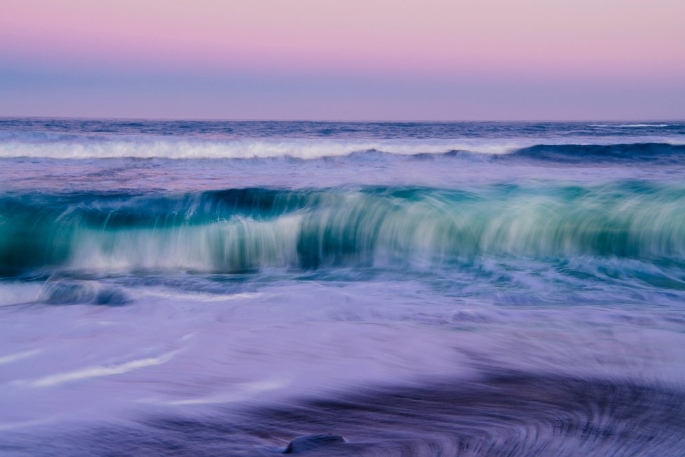 Ocean waves crash along the shoreline under a pink and purple twilight sky in northern Oregon and, California, USA.