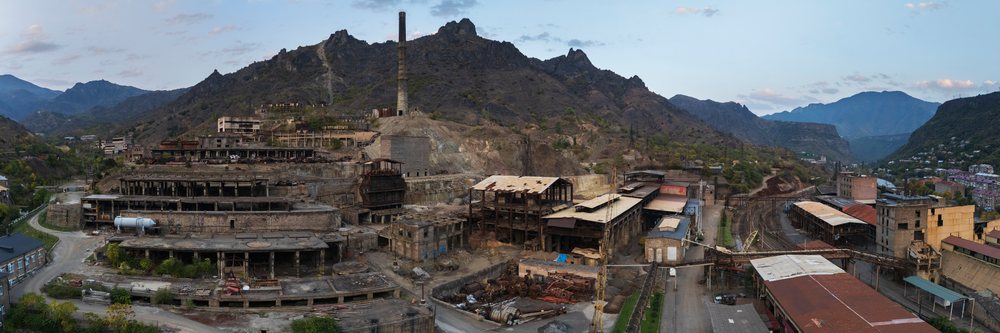 Historic copper mine ruins with industrial buildings, chimney, and railway tracks amid mountainous terrain, Alaverdi, Armenia.
