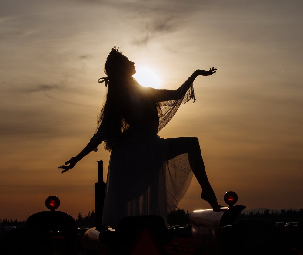 Silhouette of a woman wearing a crown and veil posing on a tractor at sunset outdoors, USA.