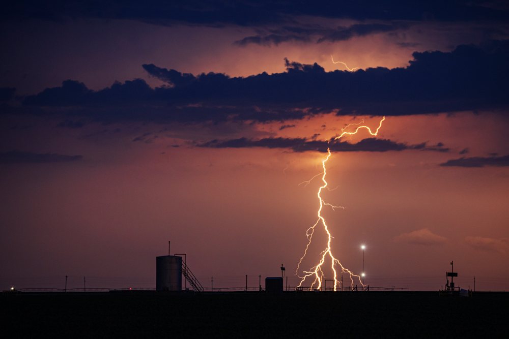 Lightning strikes down from storm clouds over a flat rural field at night, within Tornado Alley of the, Storm Chasing, Weather, Environmental issues, Great Plains, USA.